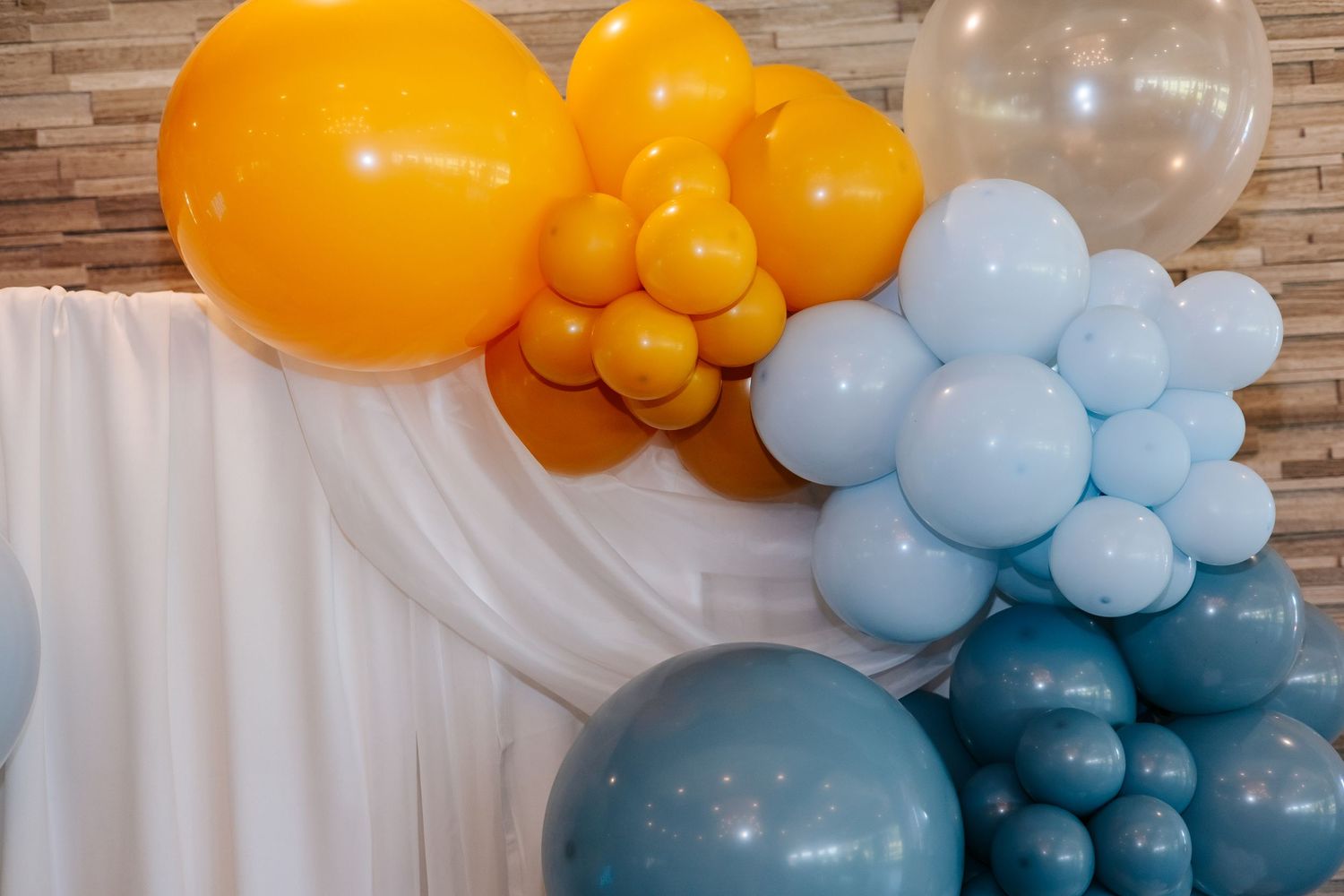 Orange and blue balloon arch decoration against brick wall.