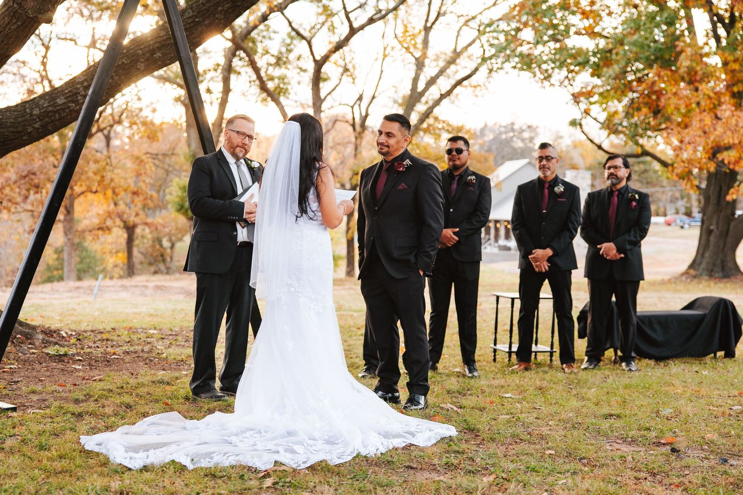 Wide angle wedding ceremony shot under autumn trees with wedding party and guests.