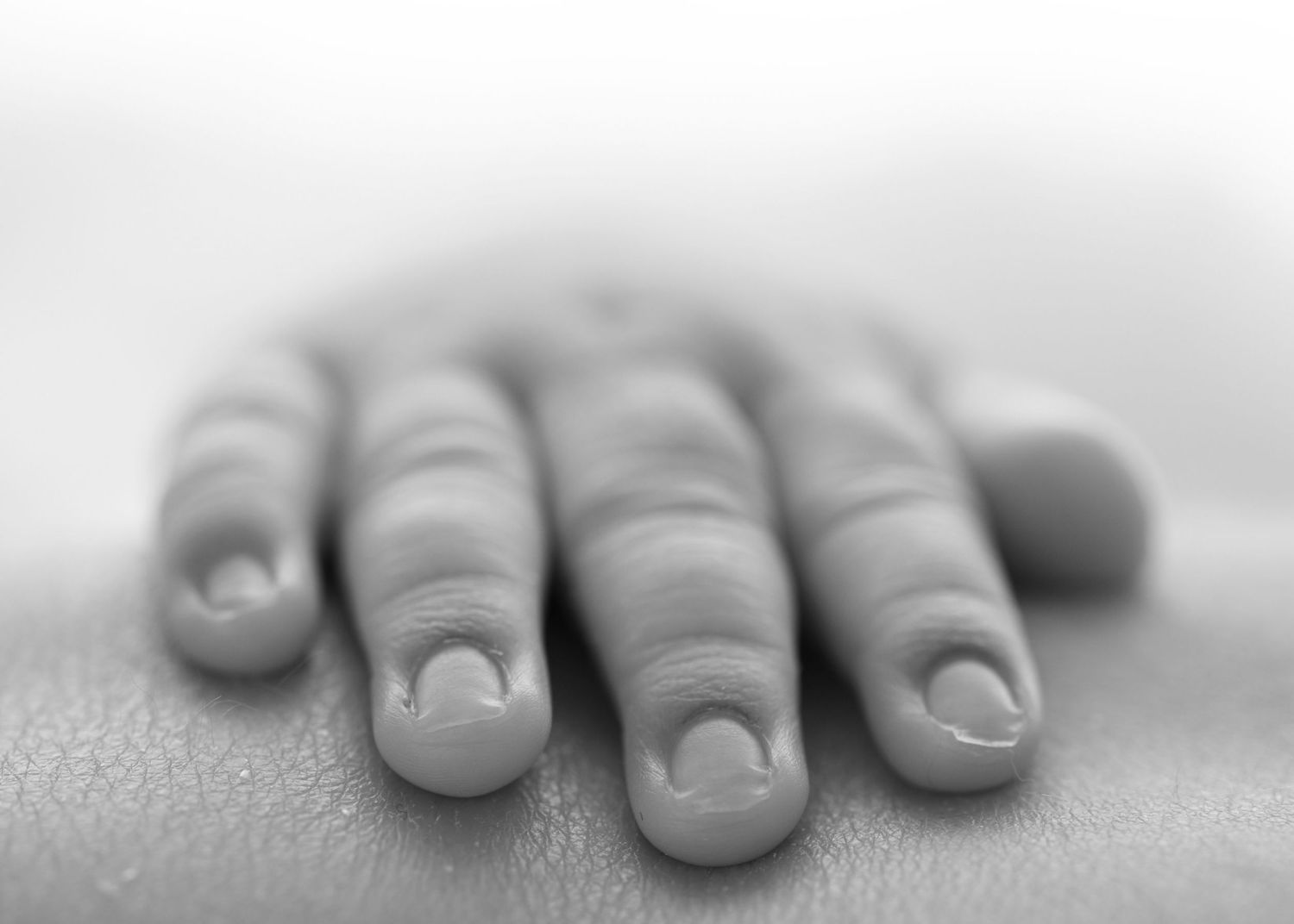 Close-up black and white photo of a baby's tiny hand with delicate fingers and nails resting on a soft surface.