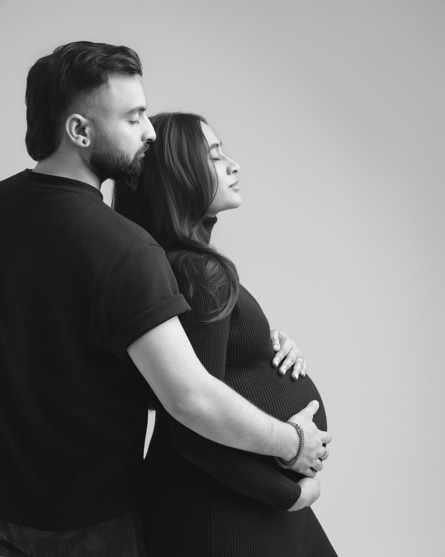 Black and white maternity photo of a couple embracing, man kissing womans head while cradling her pregnant belly.