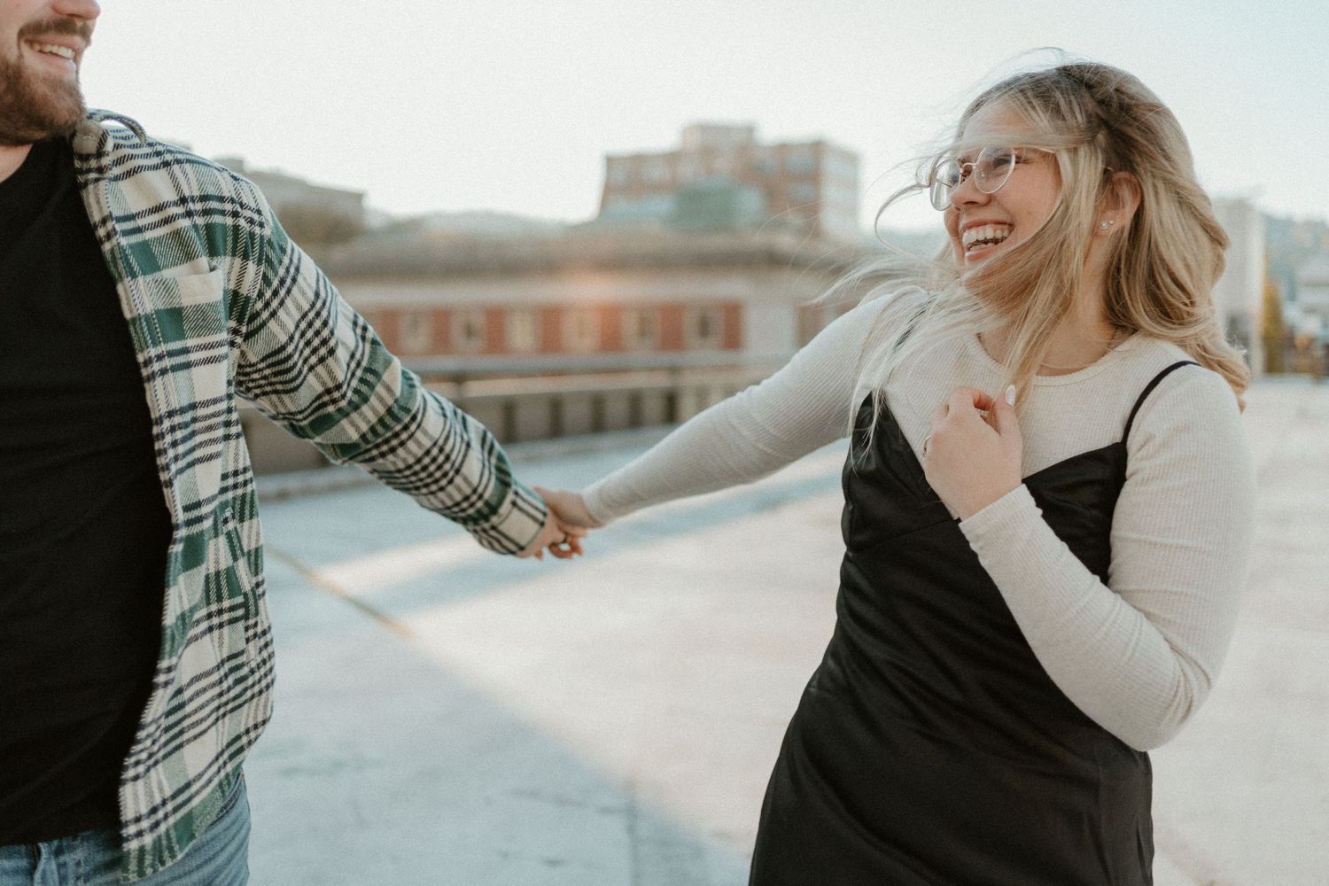 A couple holds hands during a romantic rooftop photoshoot in an urban setting.