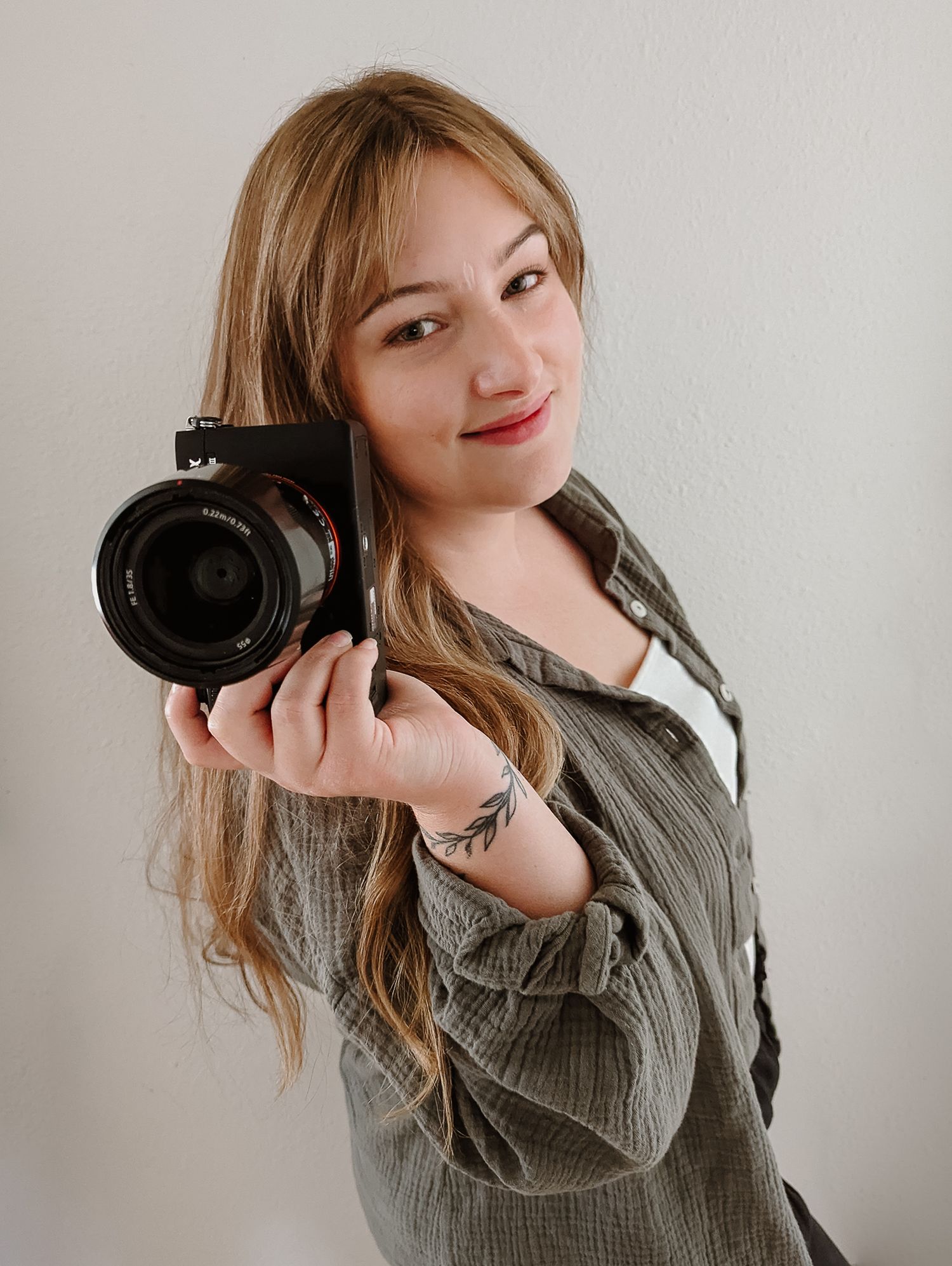A photographer poses with a professional camera against a light background.