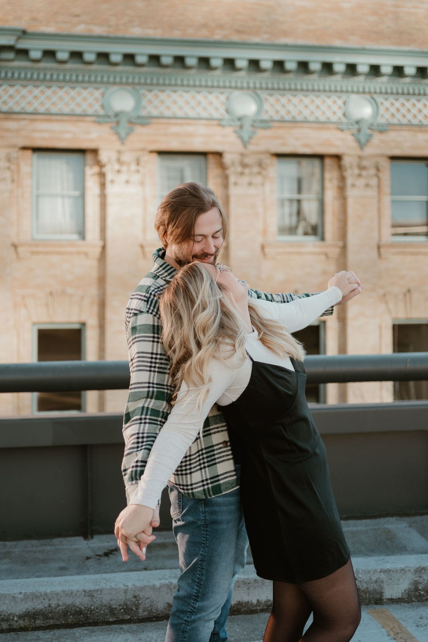 A couple embraces playfully on a rooftop with an urban backdrop during golden hour.