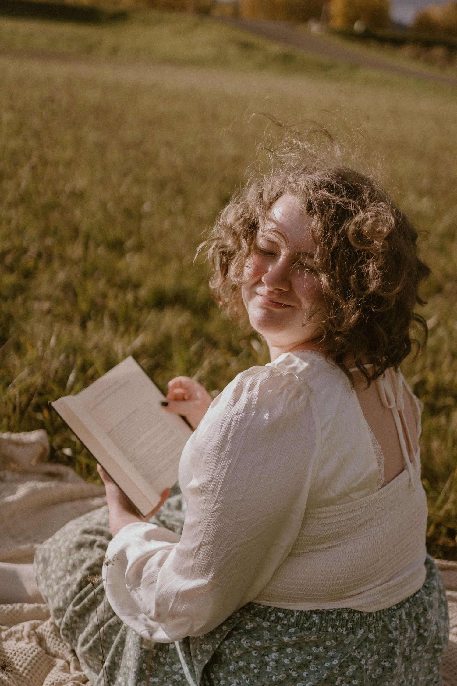 Person in white sweater relaxing outdoors with a book on a sunny autumn day.