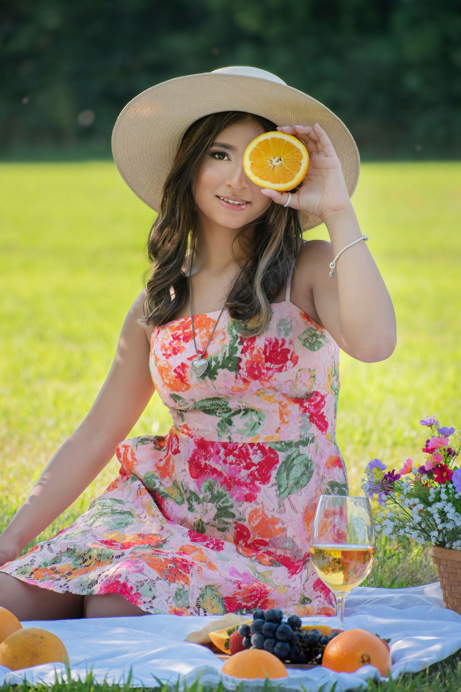 A summer picnic scene with someone in a floral dress holding an orange slice while relaxing on a white blanket outdoors.