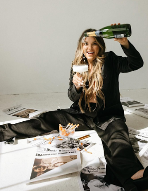 A person in black clothing lies on the floor with wine and papers scattered around in a creative photo series.