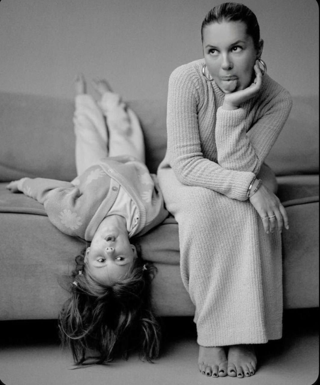 Black and white portrait of two people in cozy sweaters lounging on a sofa in casual, relaxed poses.
