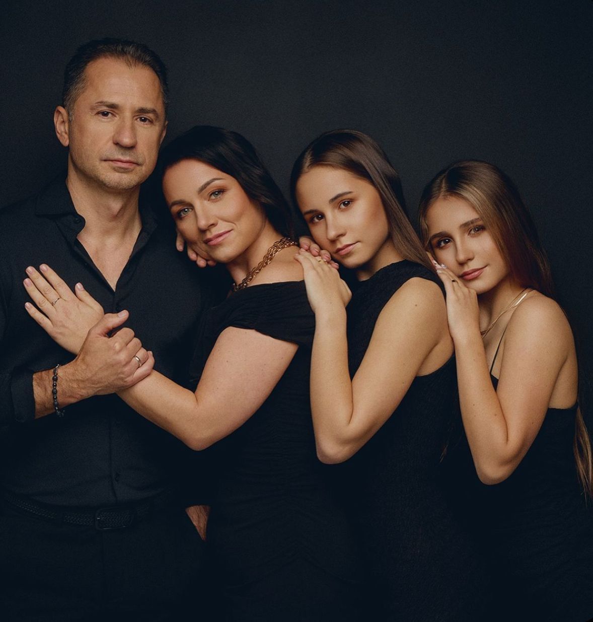 Four elegantly dressed family members in black outfits pose together against a dark studio background.