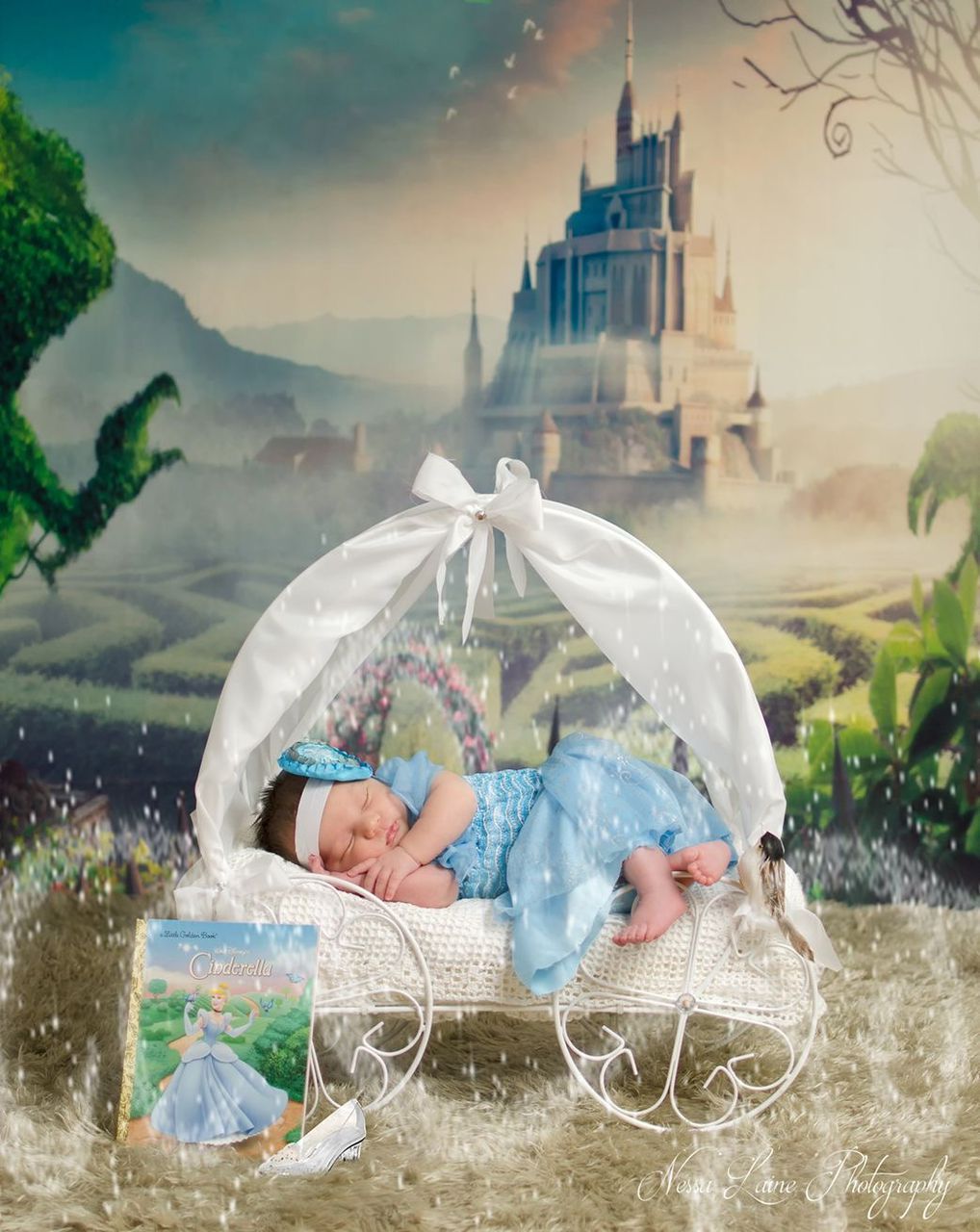 Newborn baby in blue Cinderella dress sleeping in white carriage prop with fairytale castle backdrop.
