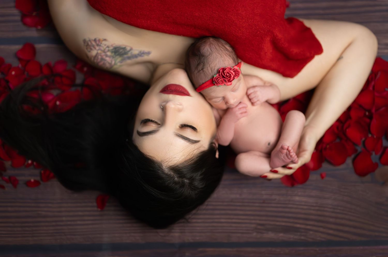 Mother and newborn portrait with red flowers and dramatic styling.