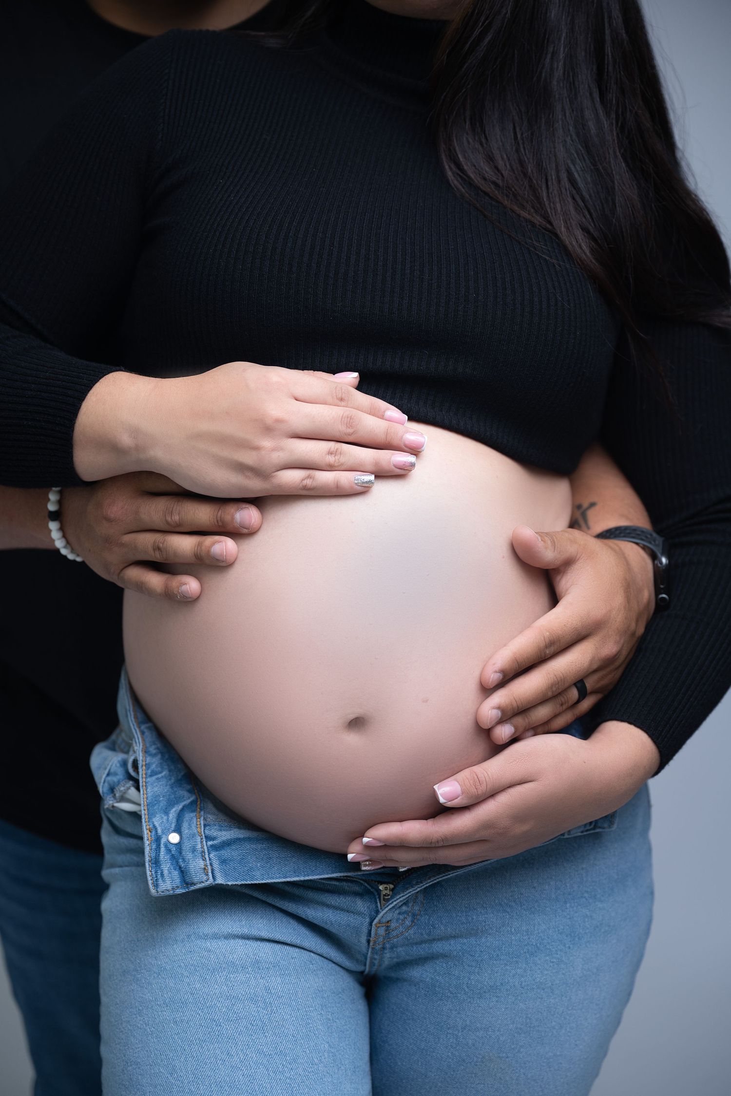 Close-up of hands cradling pregnant belly wearing black sweater and jeans.