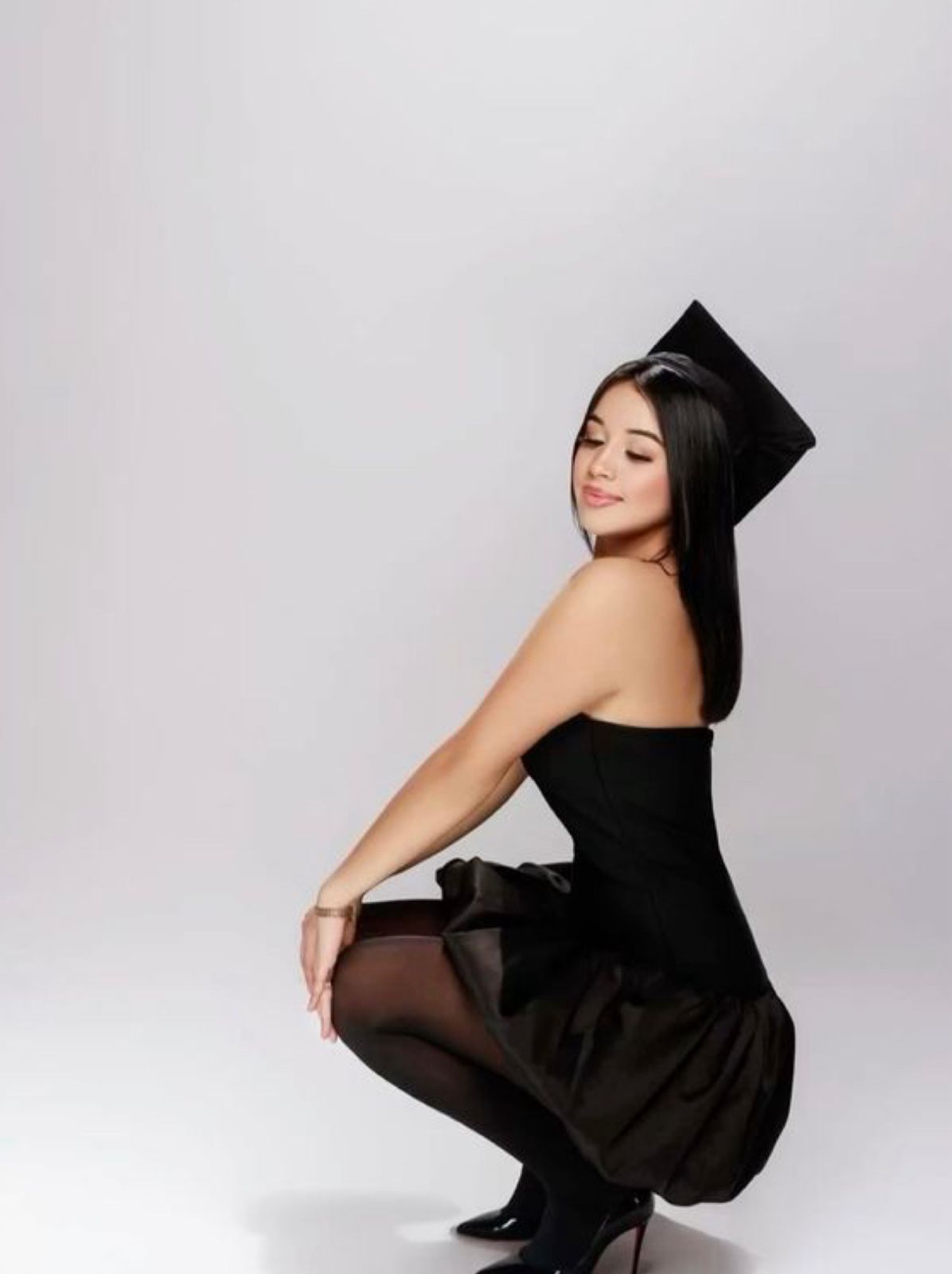 A figure in a flowing black dress and long dark hair poses gracefully against a light gray studio backdrop.