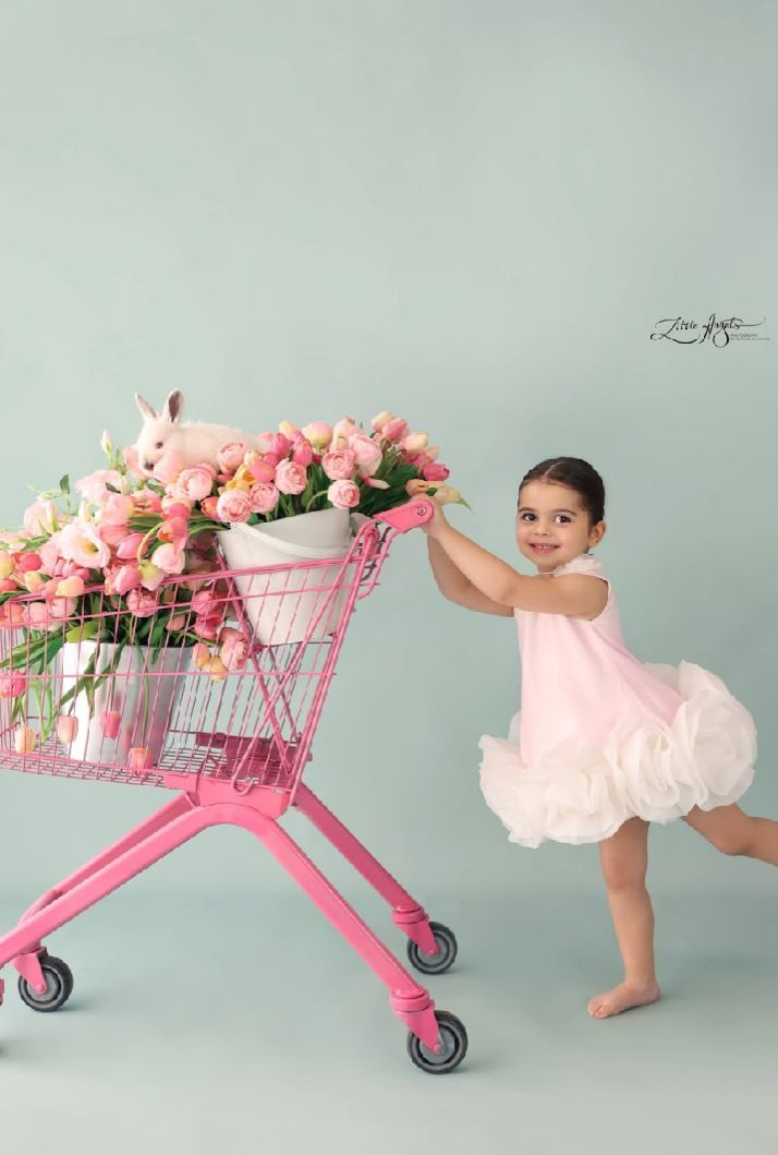 Pink shopping cart filled with fresh flowers and delicate pink decor against a light gray backdrop.