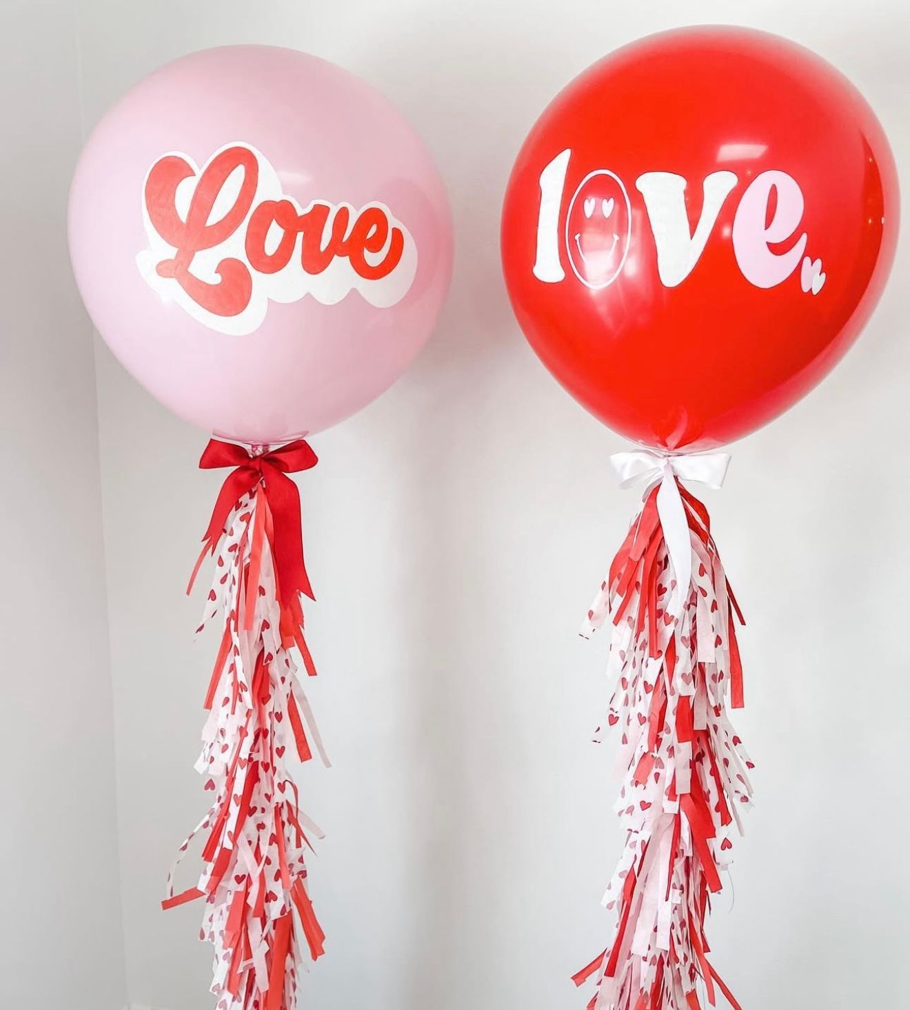 Two large Love balloons in pink and red with tassel tails, perfect for Valentine's Day party decorations.