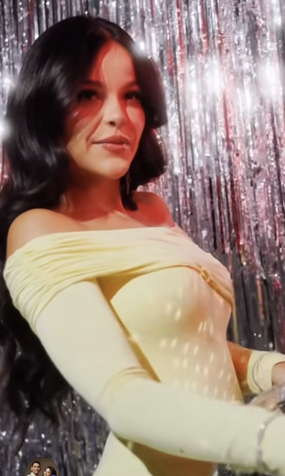 Woman in cream off-shoulder gown with long gloves poses against sparkling silver tinsel backdrop.
