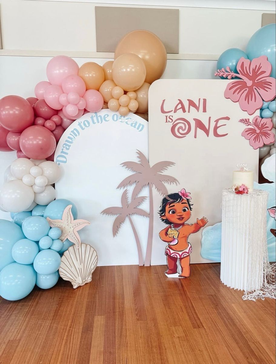 Moana-themed first birthday party decor with balloon garland, palm tree cutouts, and 'Lani is One' sign.