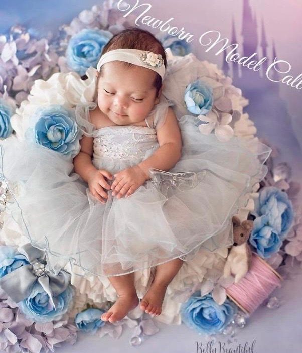 Sleeping newborn baby girl in white tutu dress with blue flowers for a newborn model calendar photo shoot.