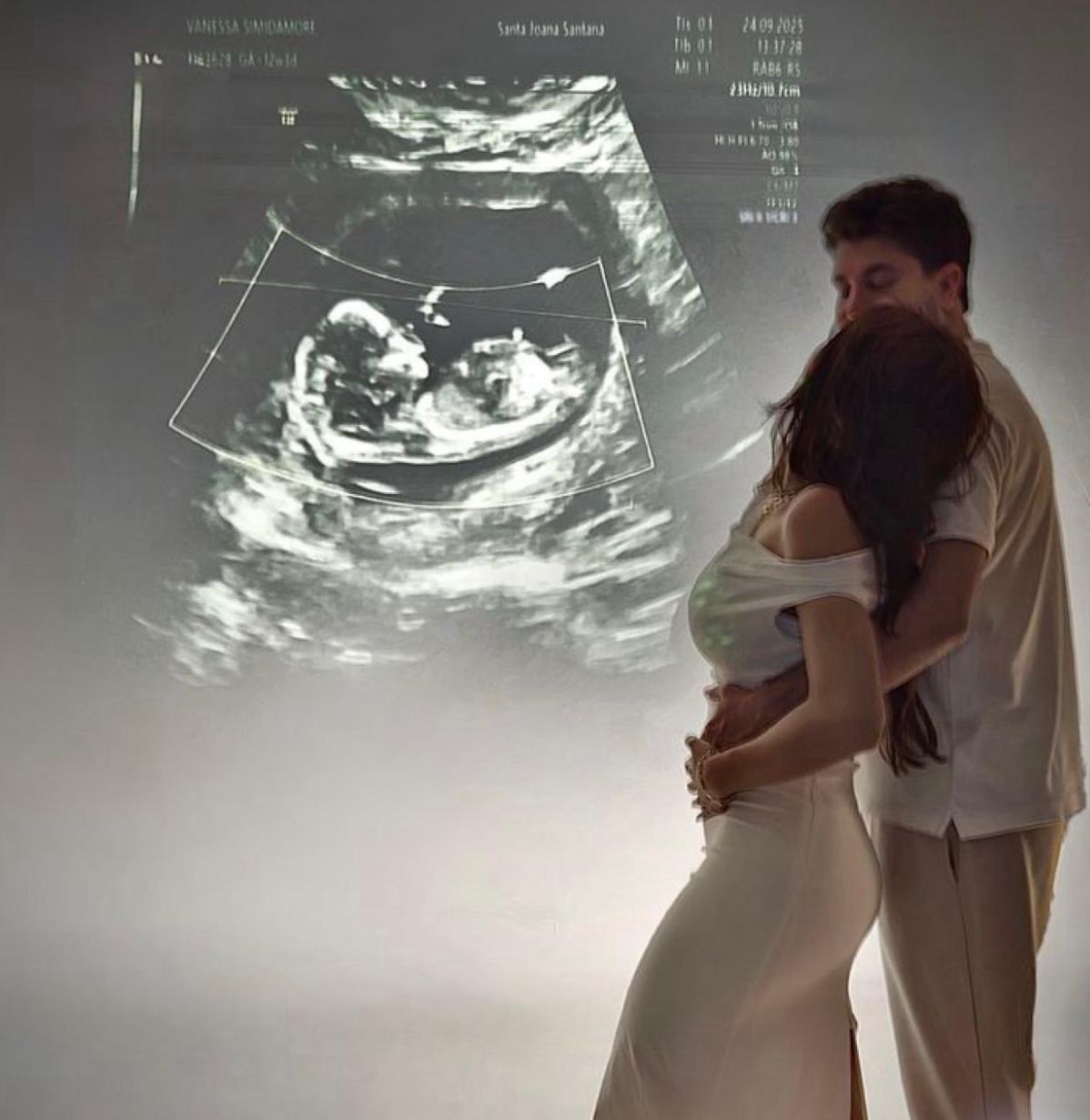 Couple embracing during maternity shoot with ultrasound image projected in background.