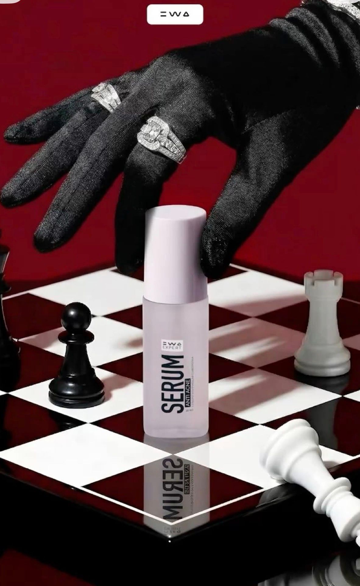 Luxury serum bottle on chess board with diamond-ringed gloved hand, red background, strategic beauty product display.