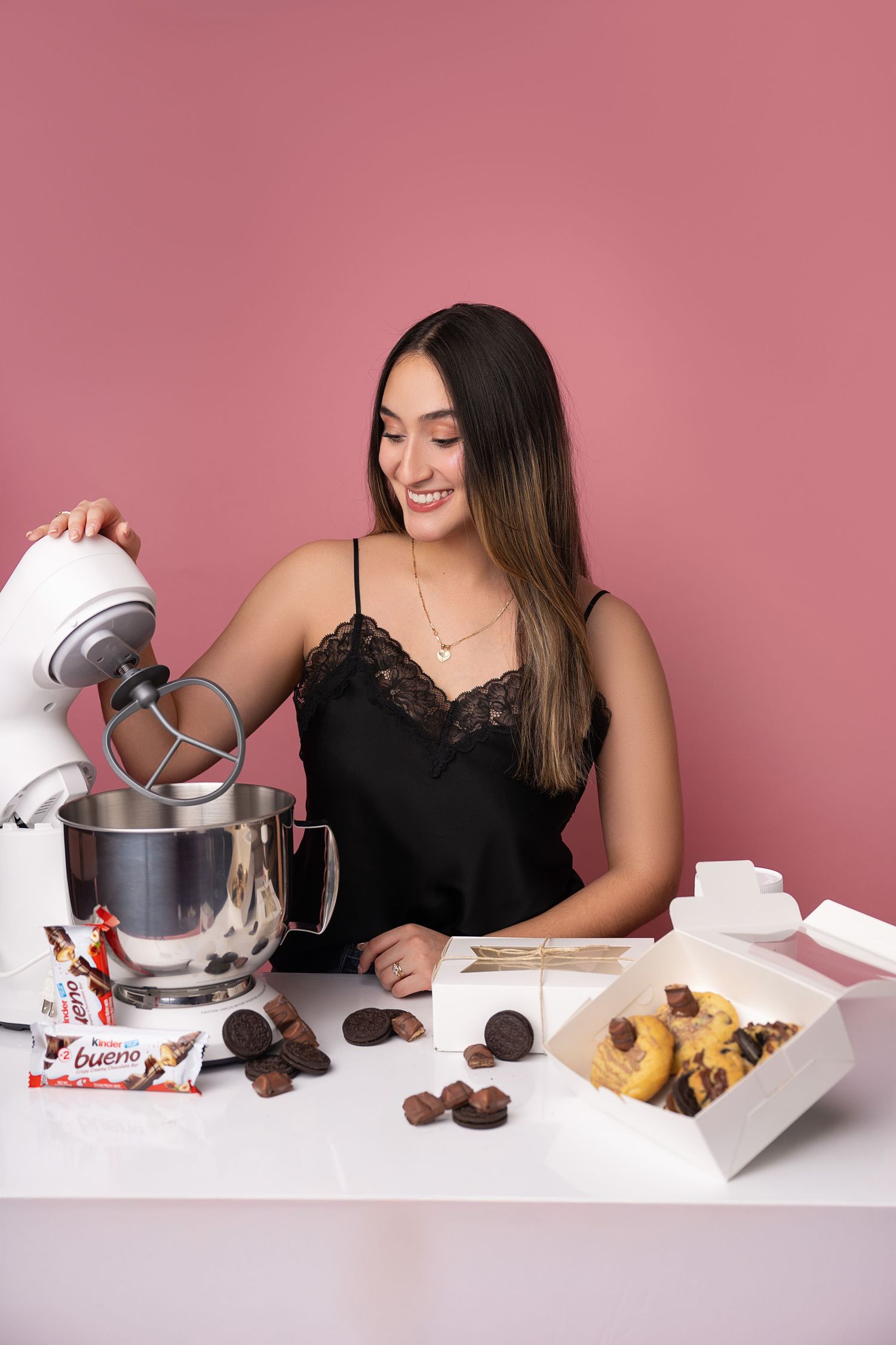Person baking with stand mixer and chocolate ingredients on pink background.