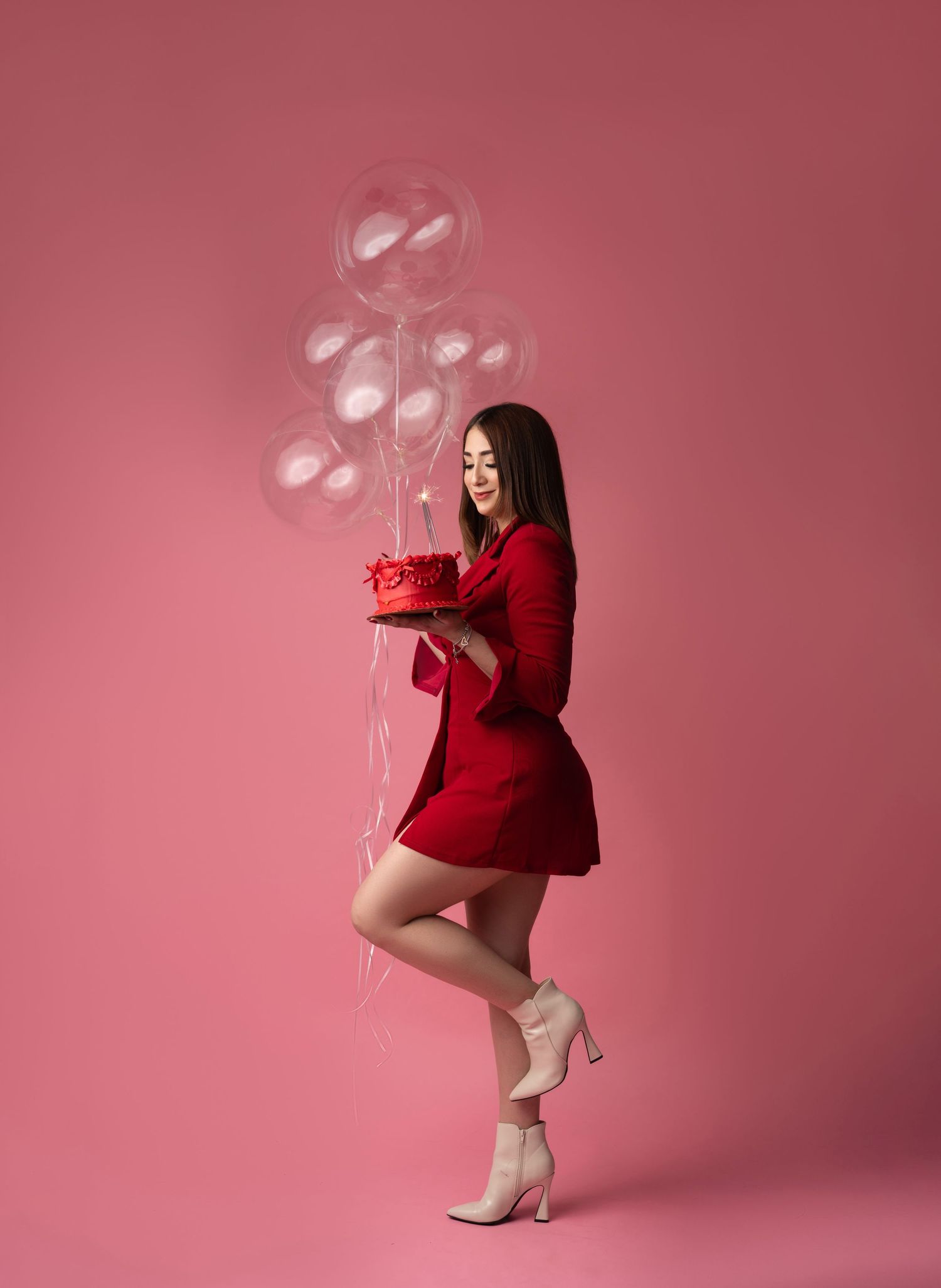 Festive scene with transparent balloons and red dress against pink background.