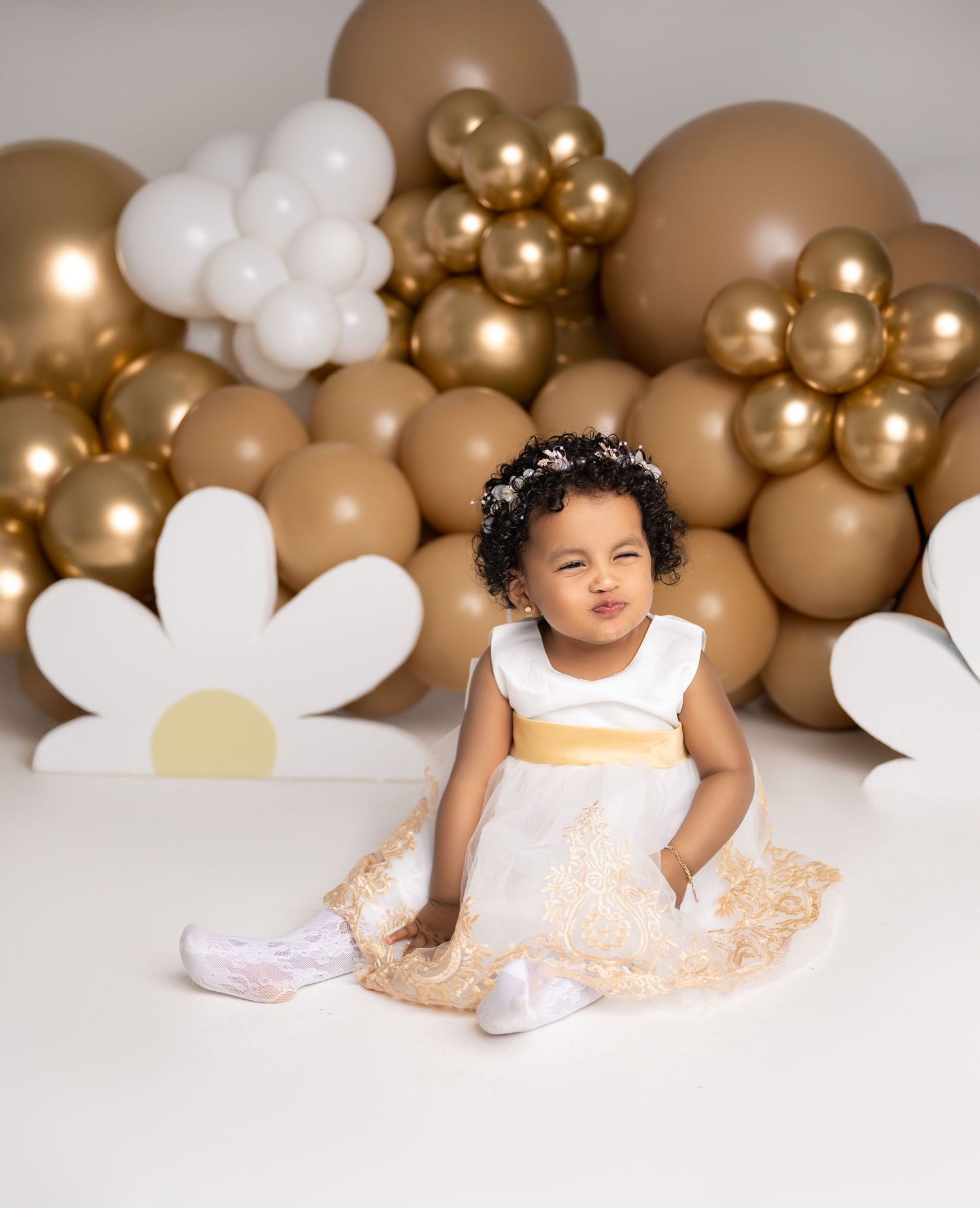 Whimsical cake smash photo setup with gold and white balloons and daisy decorations.