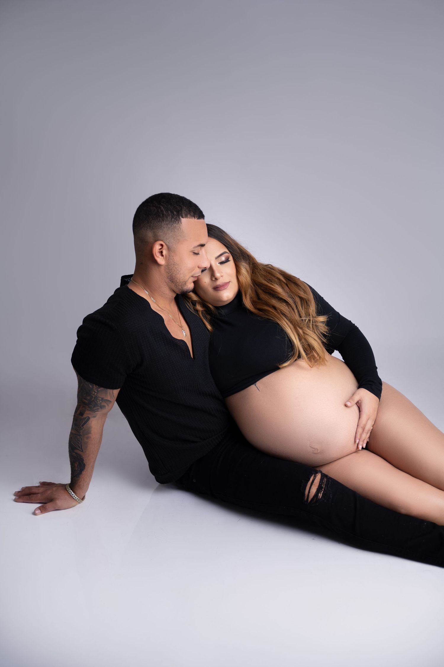Intimate maternity portrait with couple in black clothing on light background.