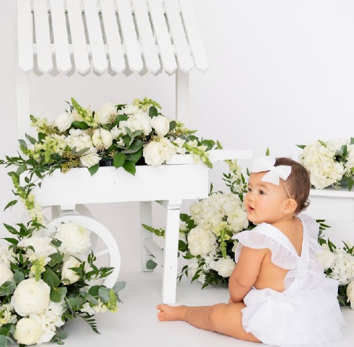 A white decorative bench adorned with elegant white roses and greenery in a dreamy studio setting.