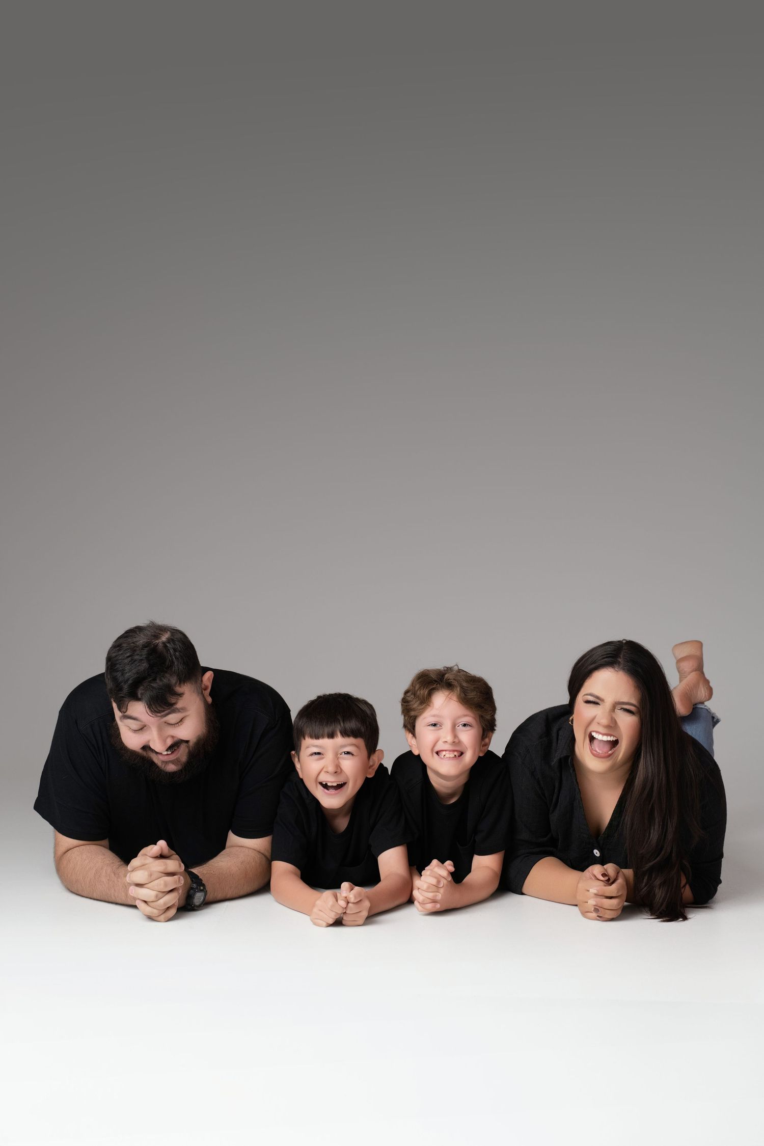 Family of four in black shirts lying on floor smiling at camera in studio portrait.