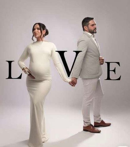 Elegant maternity photo shoot with couple in white outfits holding hands between large LOVE letters.