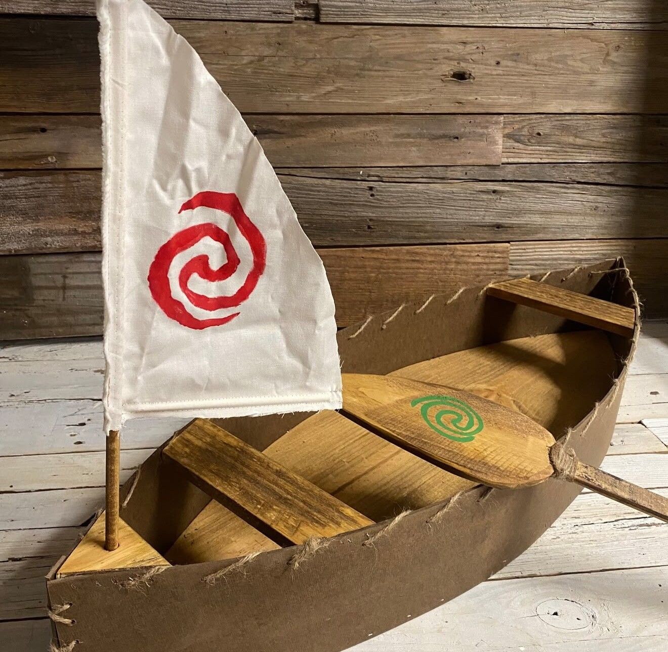Handmade cardboard Moana sailboat prop with spiral symbol flag for Hawaiian themed party.