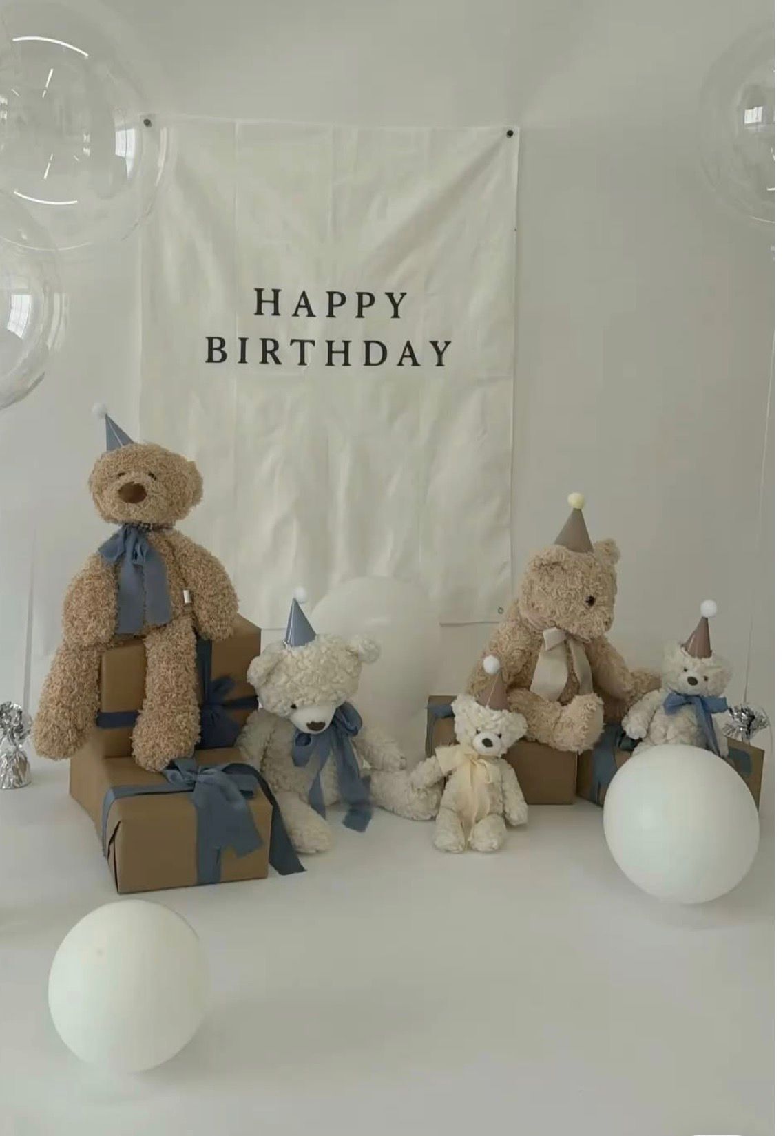 Four teddy bears with party hats and blue ribbons arranged around gift boxes near a Happy Birthday banner.