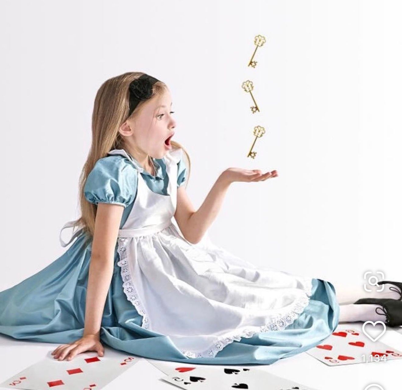 Girl in Alice in Wonderland costume sits with playing cards, catching golden keys floating in the air.