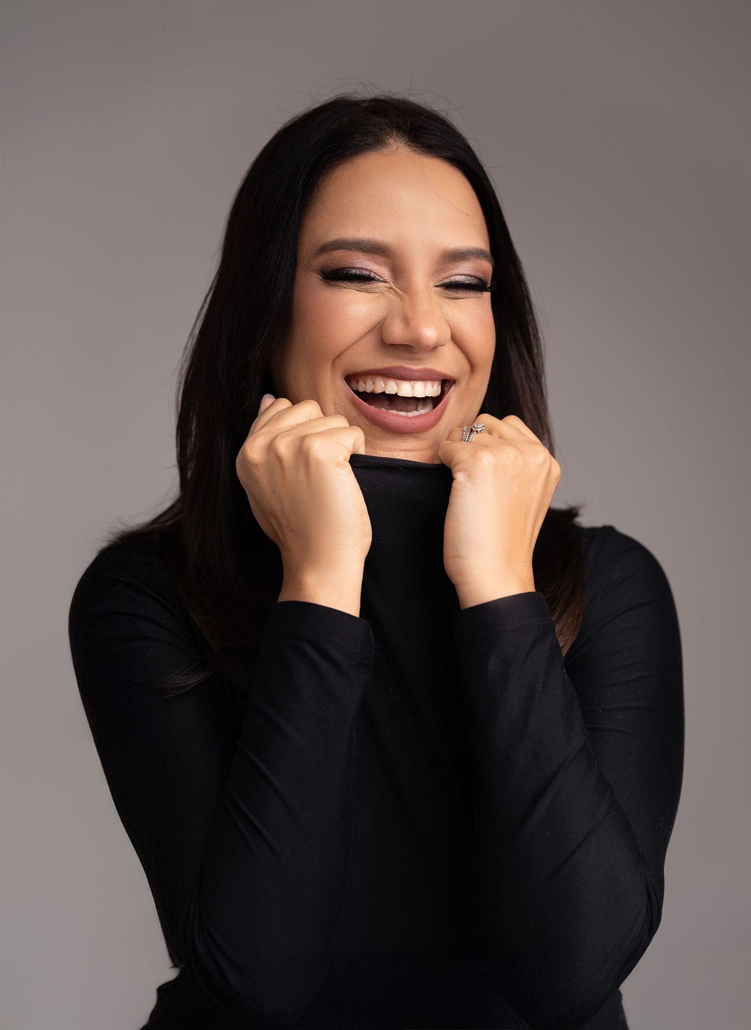 A joyful expression of happiness wearing a black turtleneck sweater against a gray studio background.