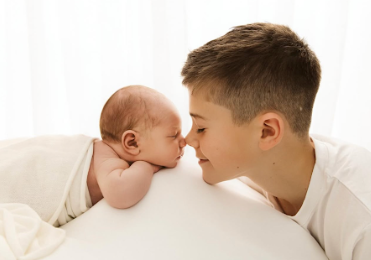 A parent and baby share an intimate bonding moment while lying together on white bedding.