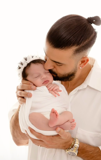 Parent in white shirt holding sleeping newborn against bright white background.