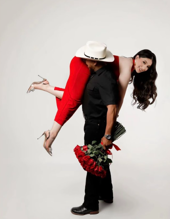 A couple in a romantic pose with red roses, featuring a red dress and cowboy hat against a white background.