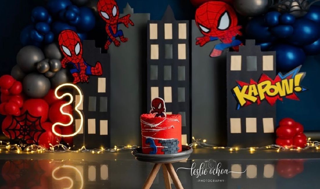 Spider-Man themed party setup with cityscape backdrop, balloons, and illuminated decorative elements.