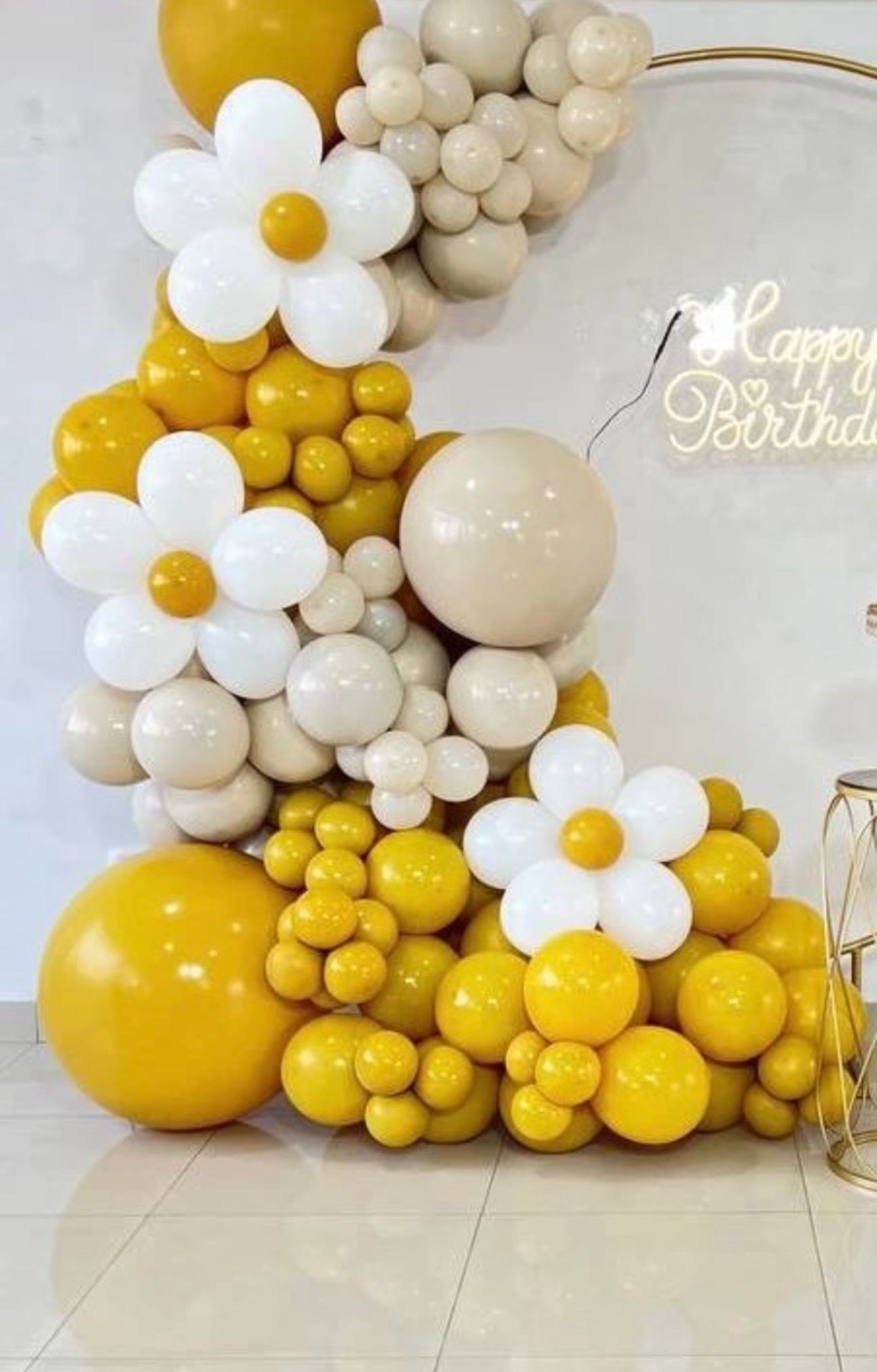 Yellow and white balloon garland with daisy flower designs creates a cheerful party backdrop against a light wall.