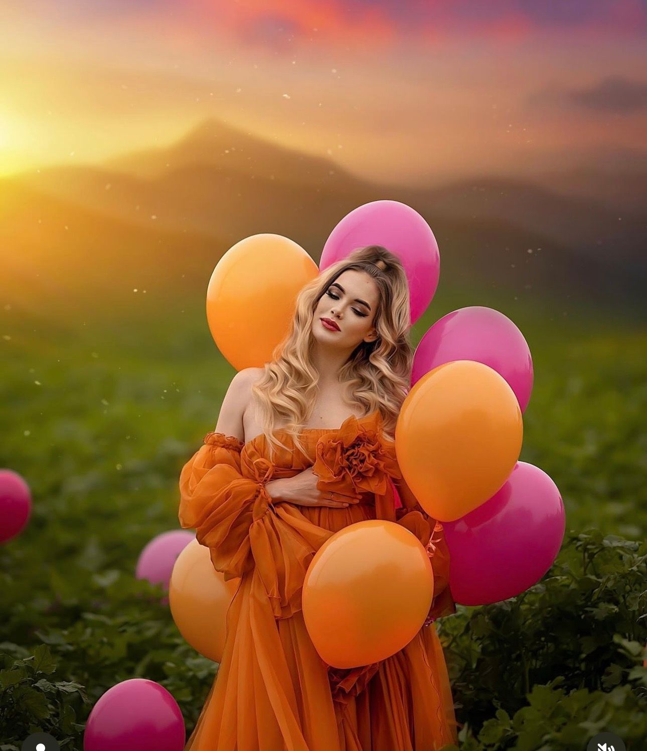 Woman in orange gown holding colorful balloons at sunset with mountain backdrop.