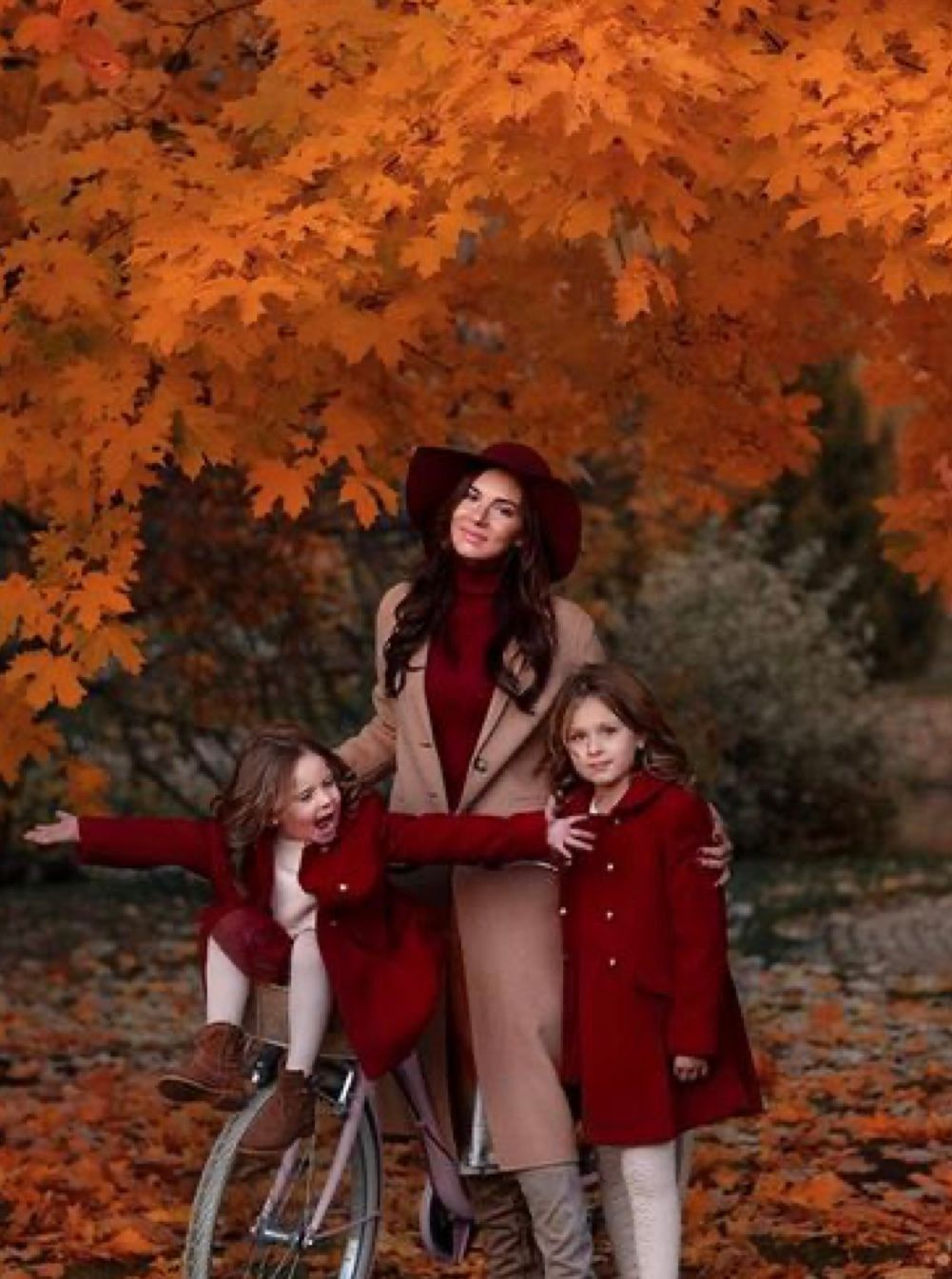Autumn scene with humans in burgundy and beige outfits against vibrant orange maple leaves in a park setting.