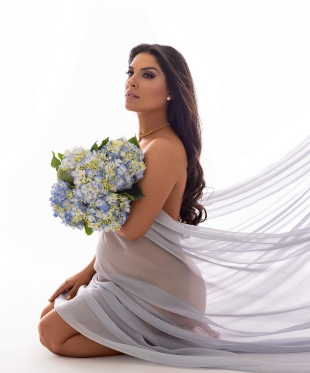 A woman in a flowing gray fabric poses gracefully against a white backdrop with blue hydrangea flowers.