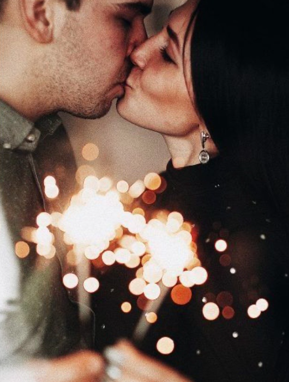 A romantic couple kissing with soft bokeh lights and sparkles creating a dreamy, intimate atmosphere in the background.