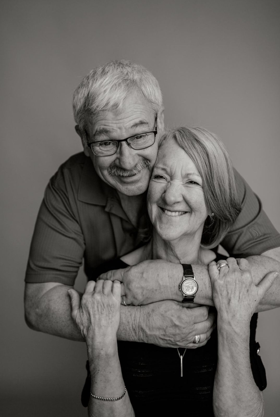 Black and white portrait of a smiling elderly couple embracing warmly in a studio setting.