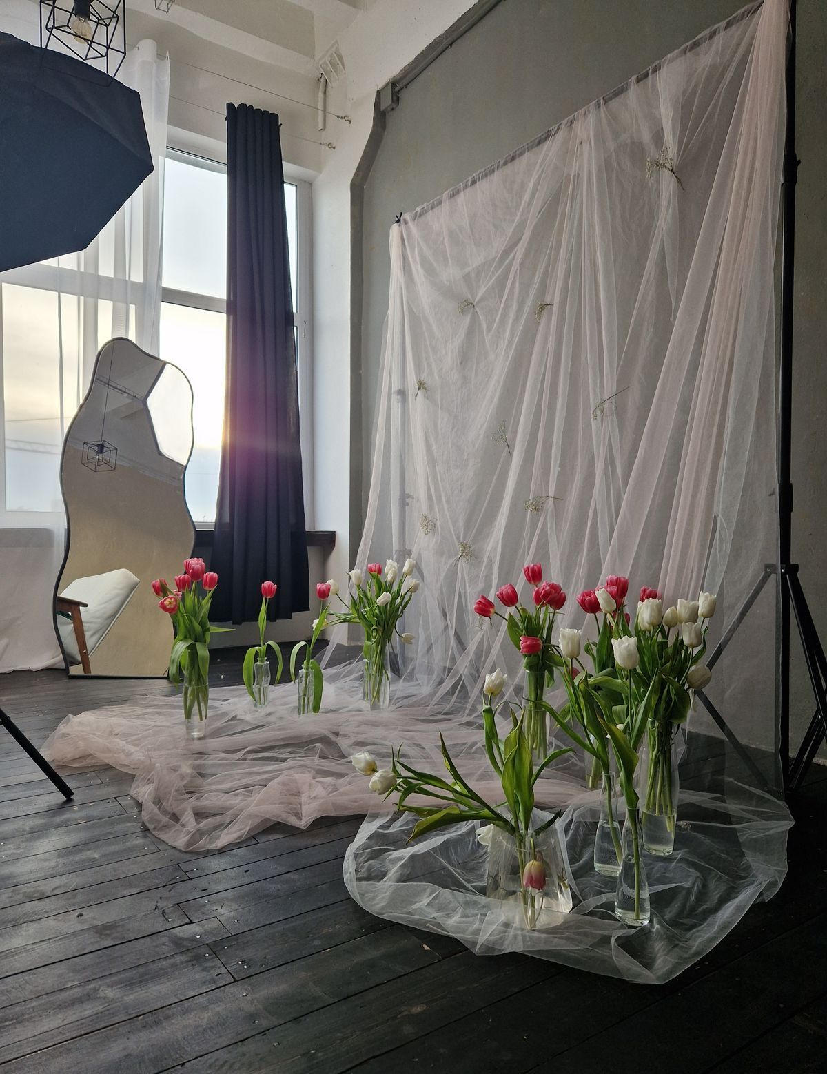 A photography studio setup with white tulips and pink tulips in glass vases arranged on sheer fabric with a backdrop.