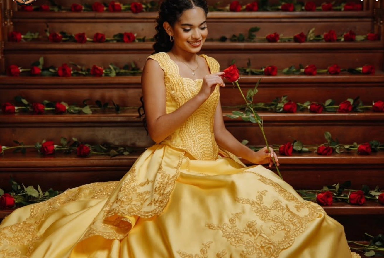 Woman in golden Belle gown holding red rose on rose-adorned staircase, Beauty and the Beast princess cosplay.