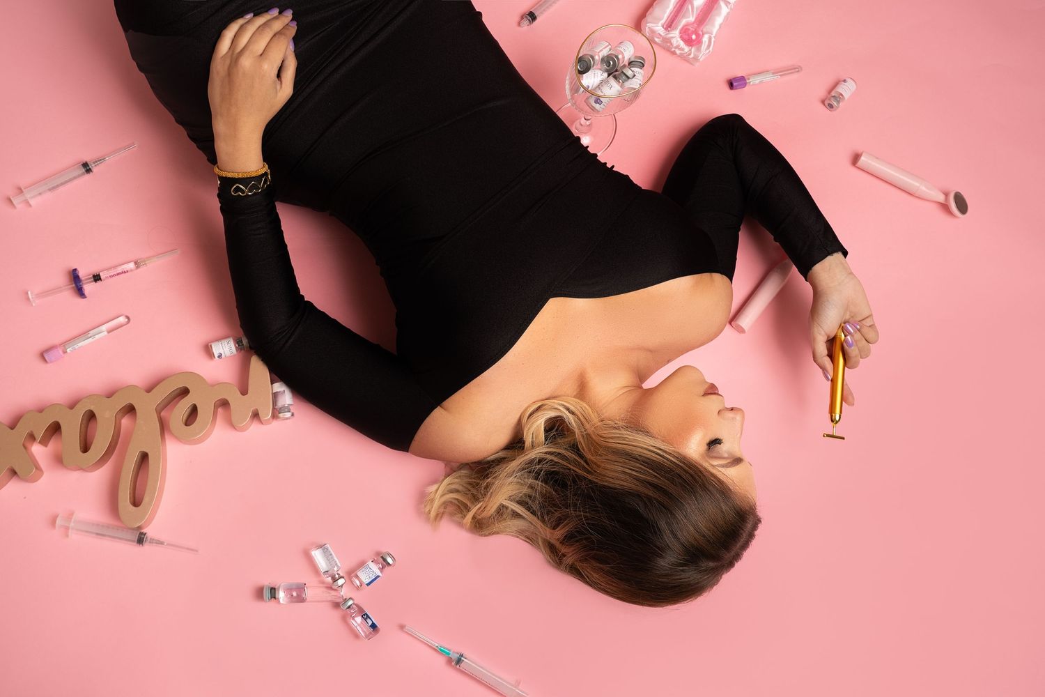 Overhead view of person in black outfit lying on pink surface with scattered decorative elements.
