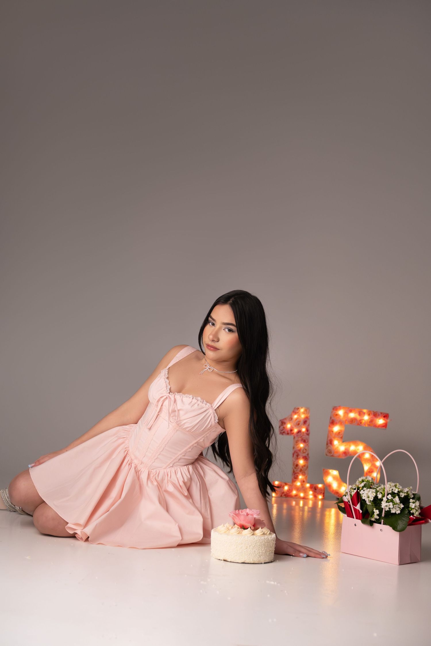Sweet fifteen birthday photoshoot with pink dress and illuminated numbers in the background.
