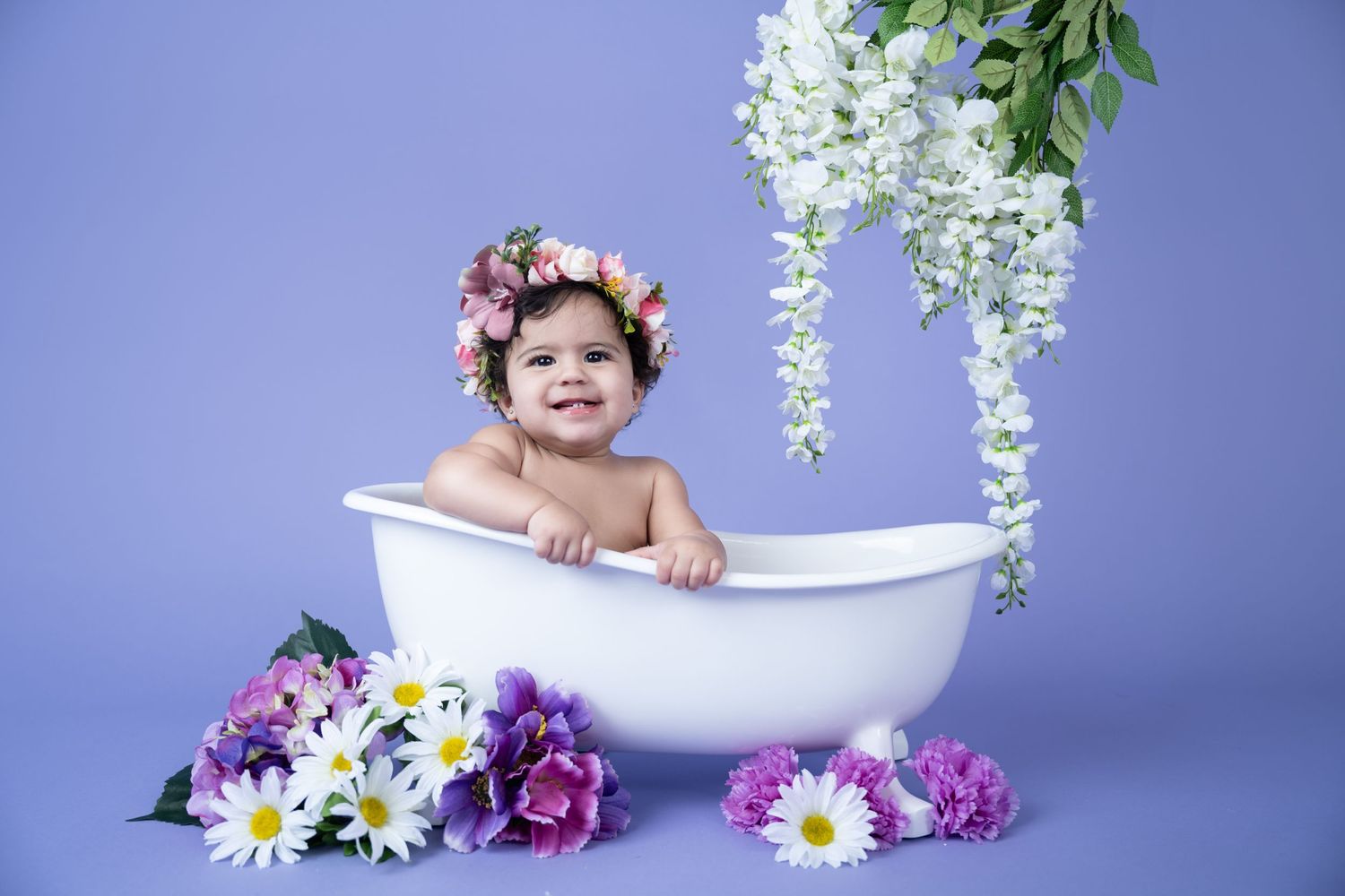 White bathtub photography setup with flowers and hanging wisteria against purple backdrop.