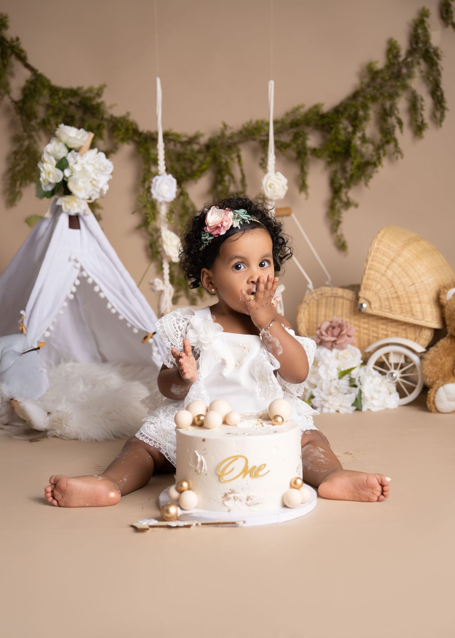 First birthday cake smash session with teepee, greenery, and floral decorations.